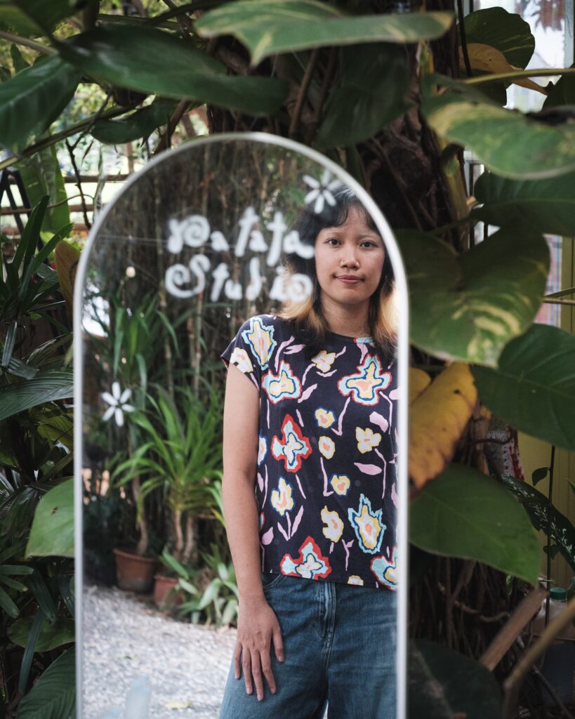Zoom reflected in an outdoor mirror among plants at Columbo Craft Village in Khon Kaen.