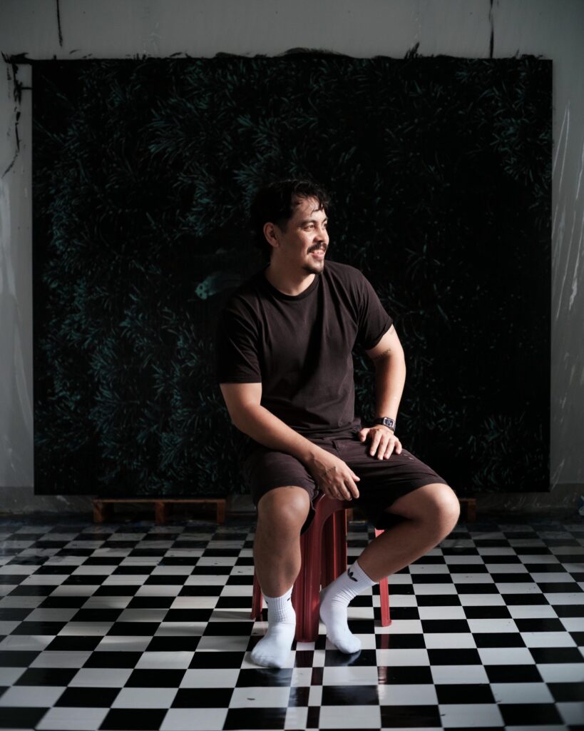 Abdul Abdullah sitting on a stool on a black-and-white chequered floor.