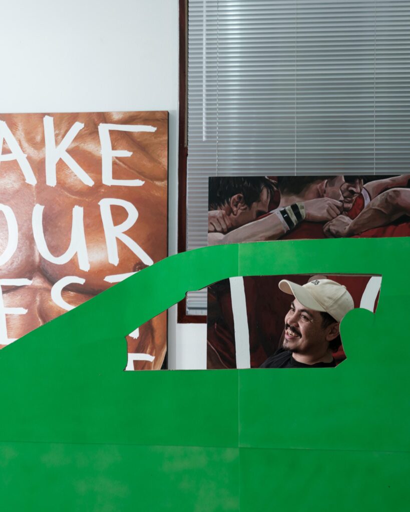 Abdul Abdullah looking through a window-shaped opening in a green car cutout.