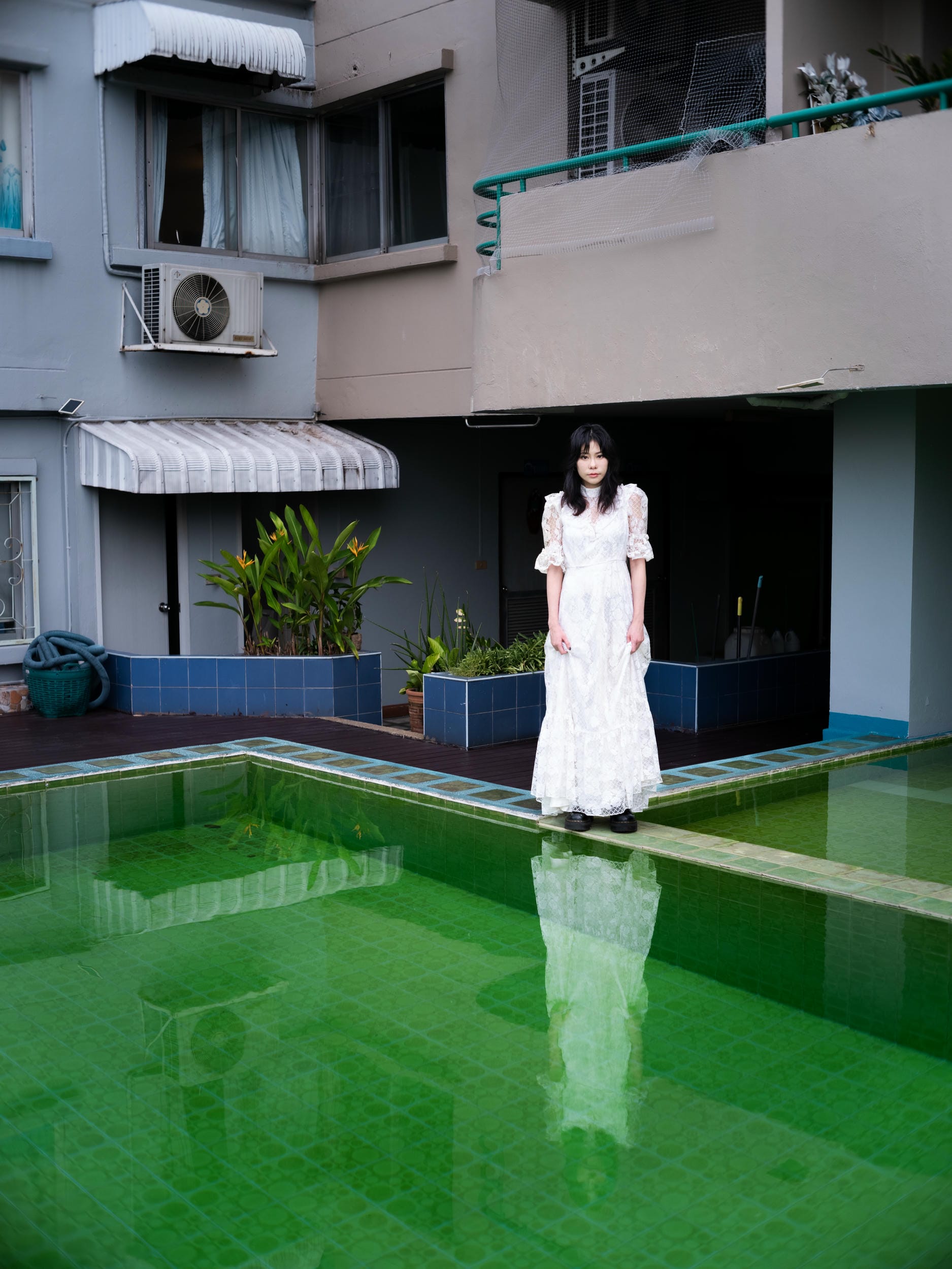 Aey Kuljira Thongkong in a white lace dress beside a green swimming pool in Bangkok.