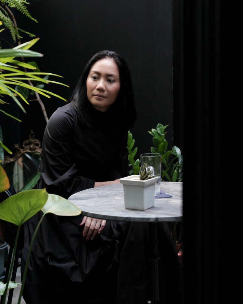 Dujdao Vadhanapakorn seated at a small table surrounded by potted plants.