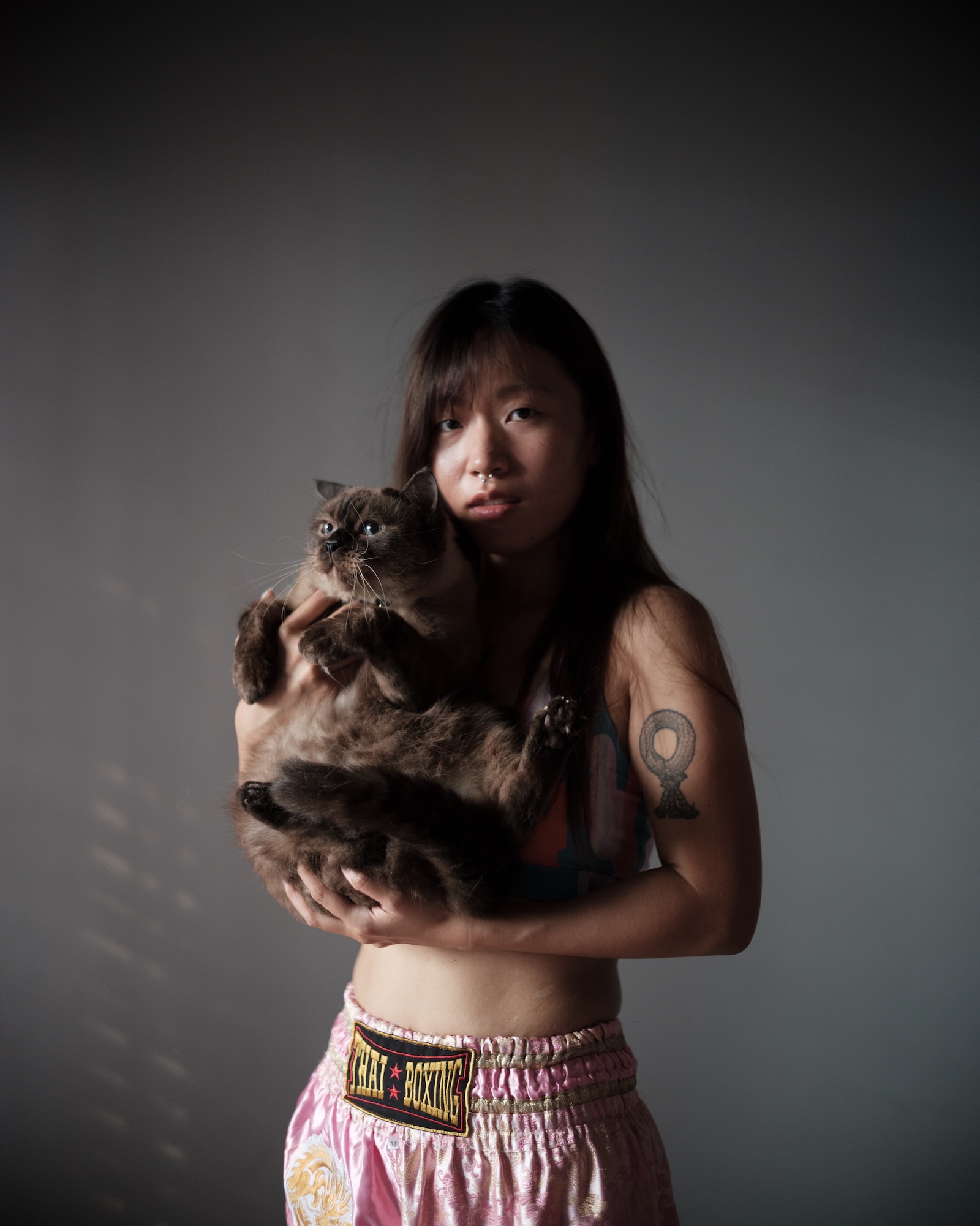 Feifei holding a cat against a dark wall