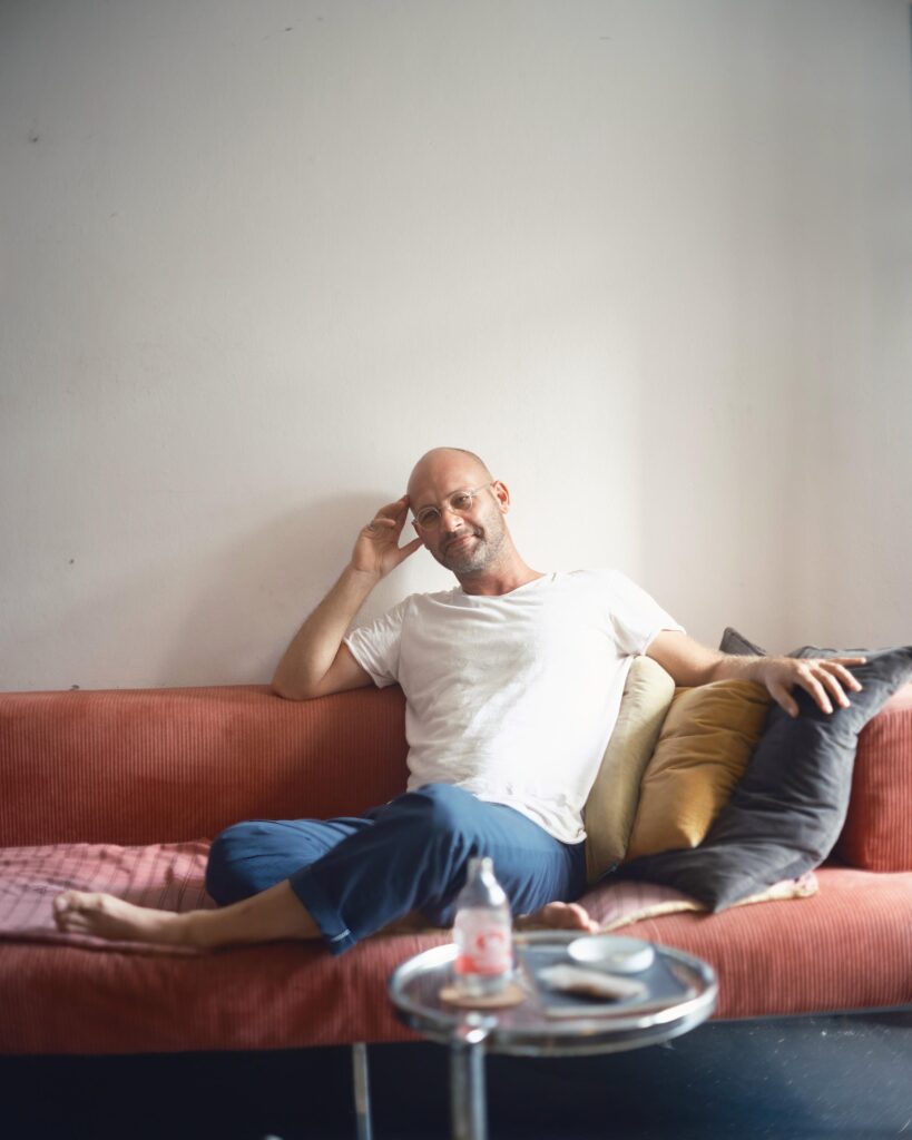 François Langella reclining barefoot on a red sofa in his Bangkok home.
