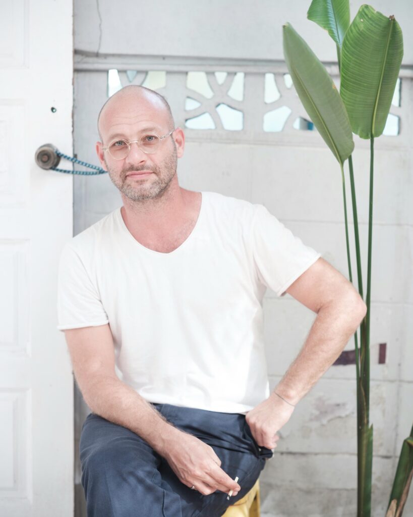 François Langella seated beside a large-leaved plant and a white door.