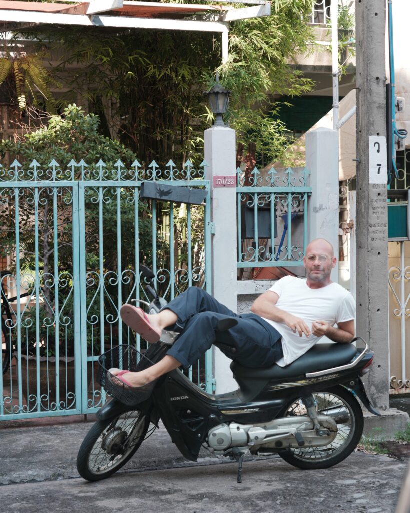 François Langella reclining on a parked motorcycle outside a Bangkok house.