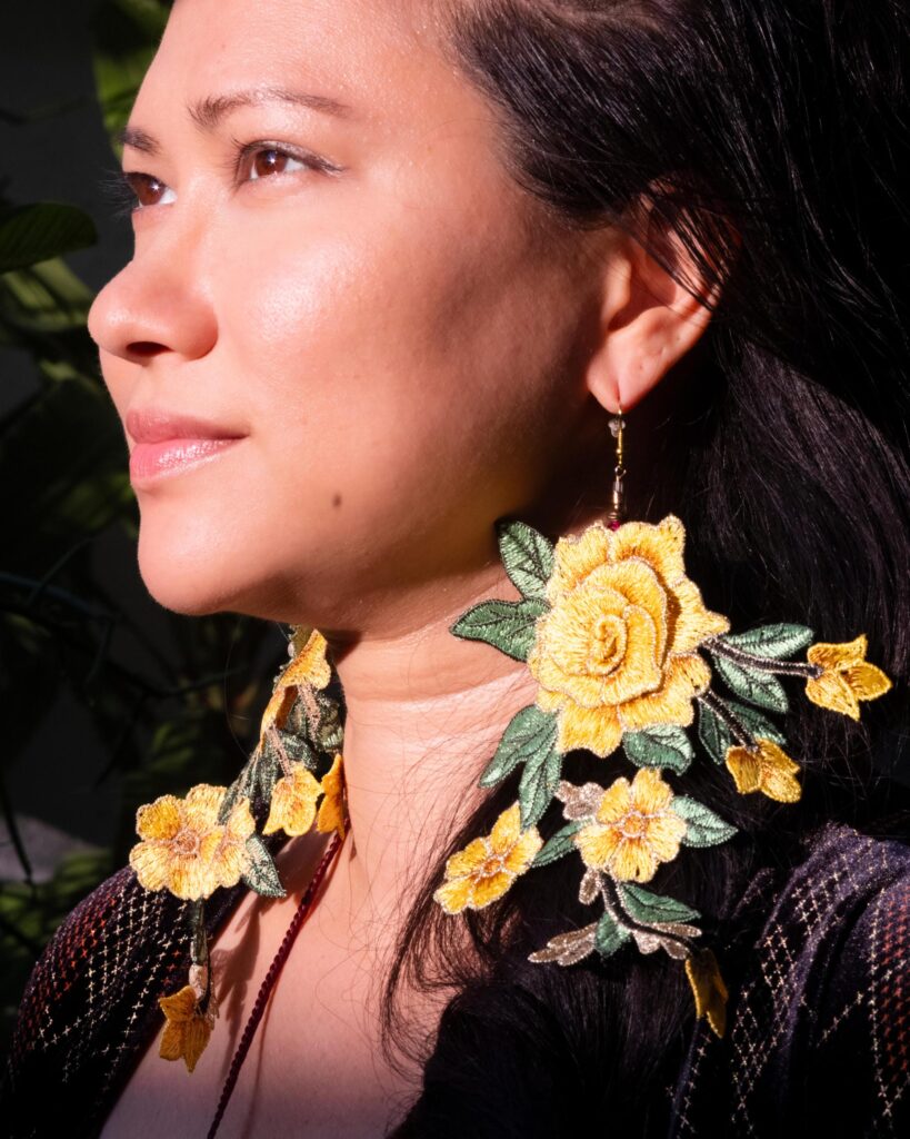 Close portrait of Gabriela Moriarty wearing large yellow flower earrings in sunlight.