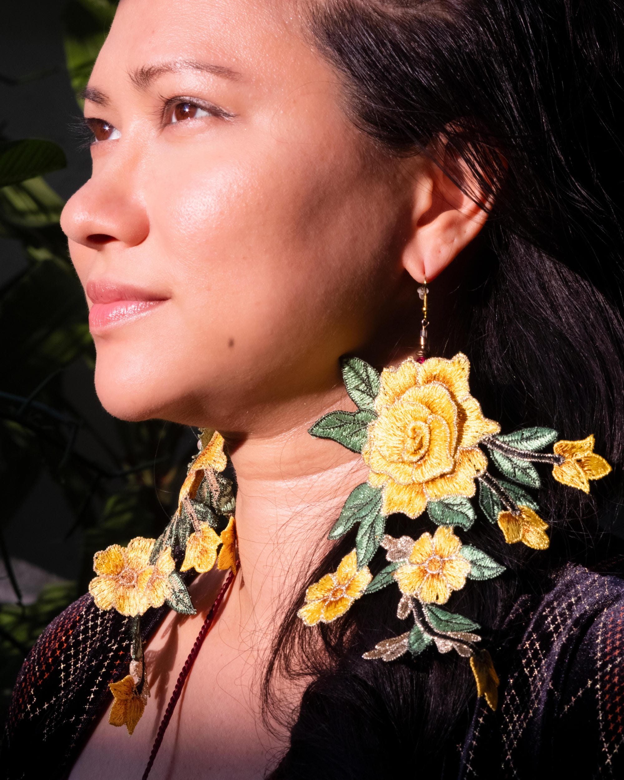 Close portrait of Gabriela Moriarty wearing large yellow flower earrings in sunlight.