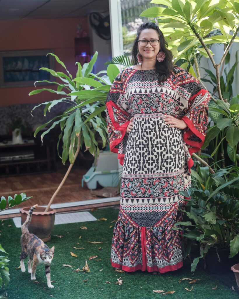Gabriela Moriarty standing among potted plants with a cat at her feet.