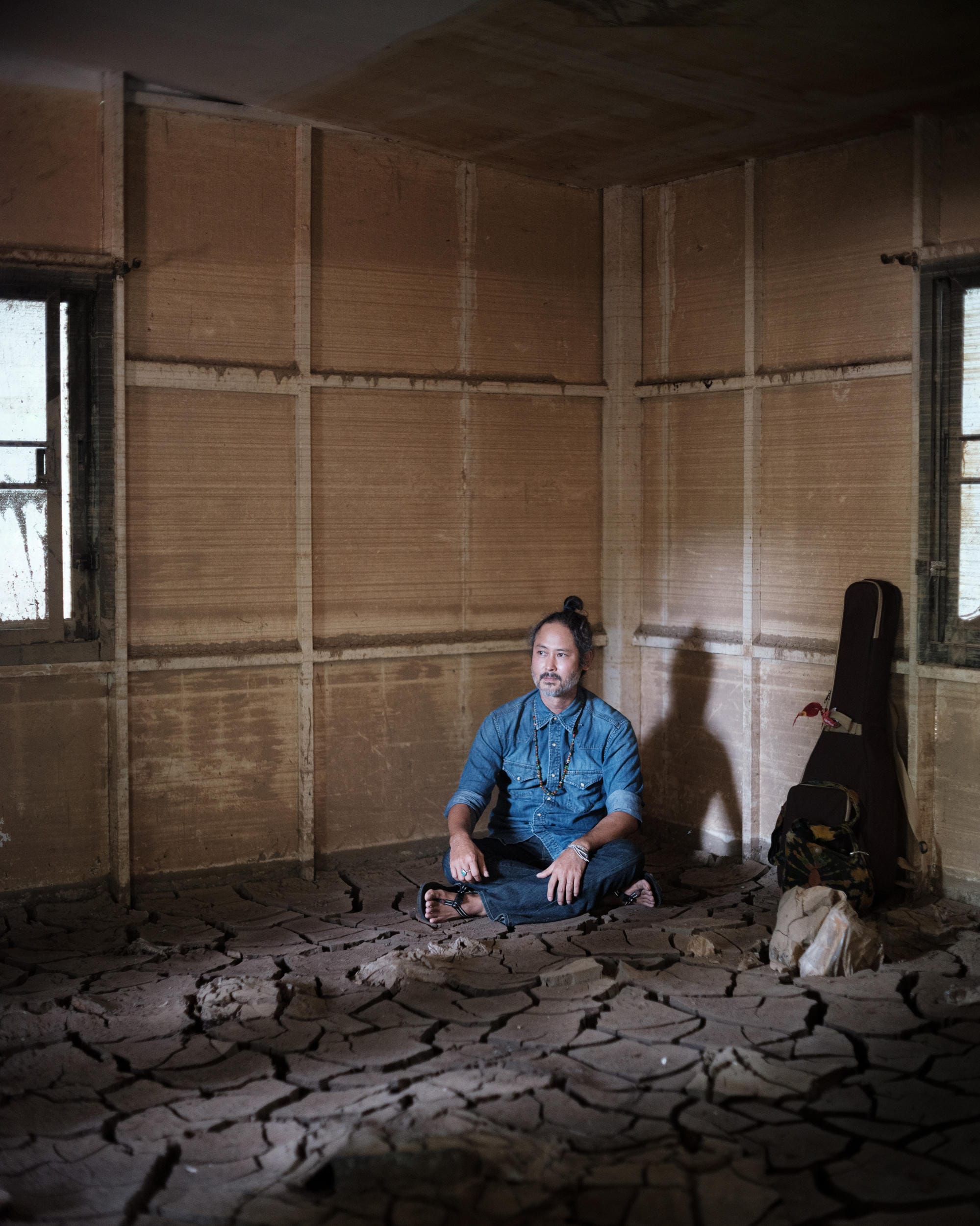 Gene Mahasmut seated on a floor covered with cracked dried mud in a Chiang Mai room.