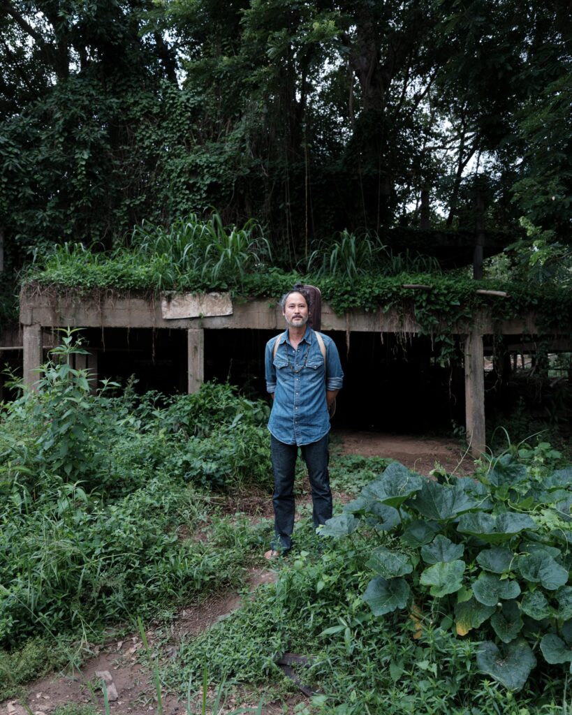 Gene Mahasmut standing among dense plants beside an overgrown concrete structure.
