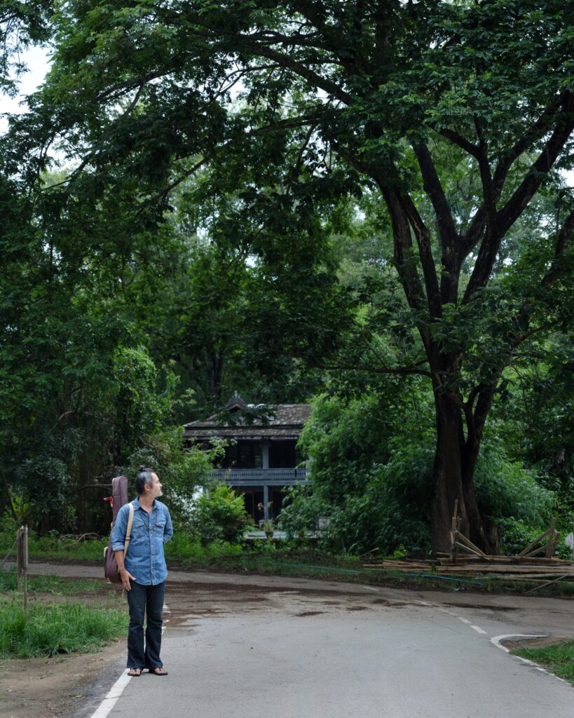 Gene Mahasmut looking up at a large tree beside a curved road.
