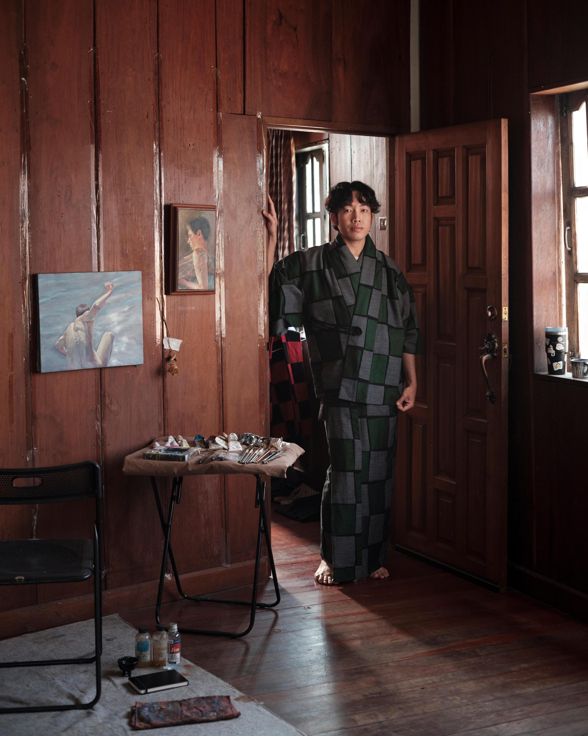 Jakkapan Mantapan standing barefoot in the doorway of his wood-panelled Phayao studio.