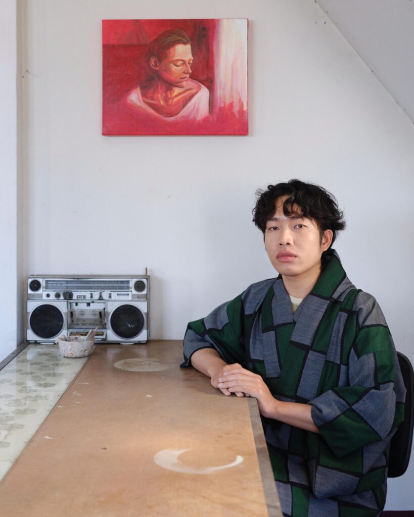 Jakkapan Mantapan seated at a table beneath a portrait painting, beside a radio.
