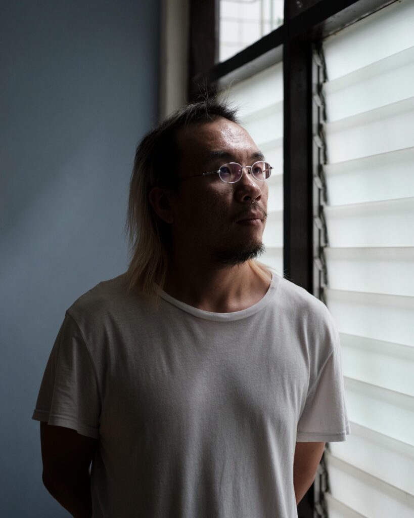 Jay Vatanakuljaras standing beside a louvred window in a white T-shirt.