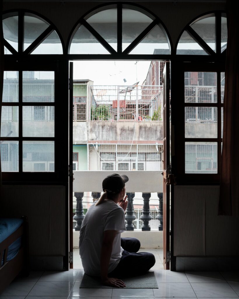 Jay Vatanakuljaras seated on the floor beside open balcony doors.