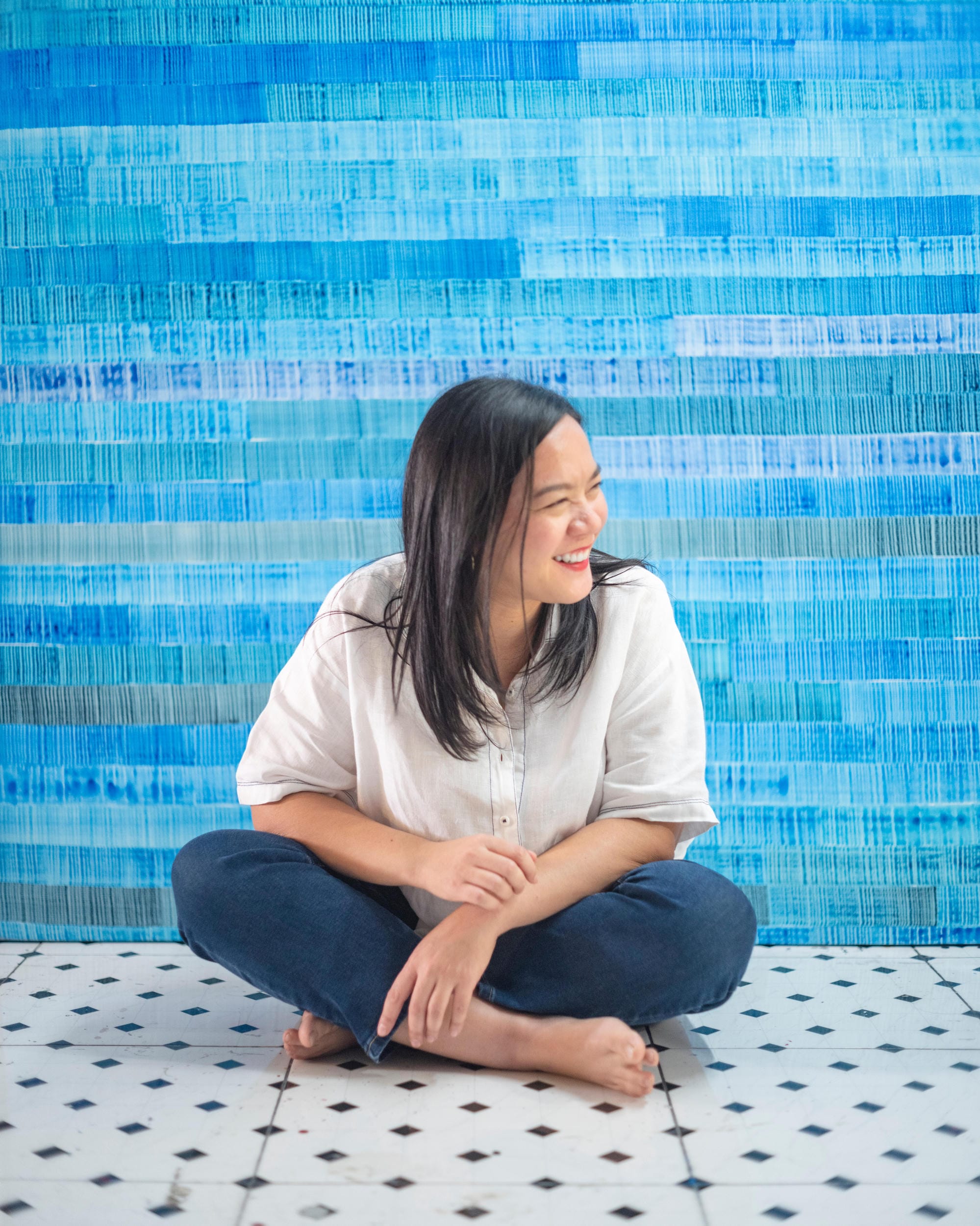 Jiratchaya Pripwai sitting cross-legged in front of a large blue painting.
