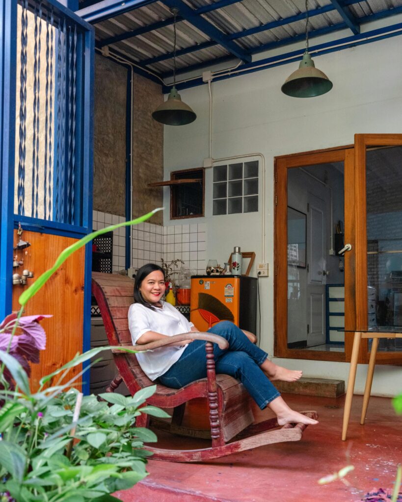 Jiratchaya Pripwai reclining in a wooden chair beside plants outside her Chiang Mai studio.