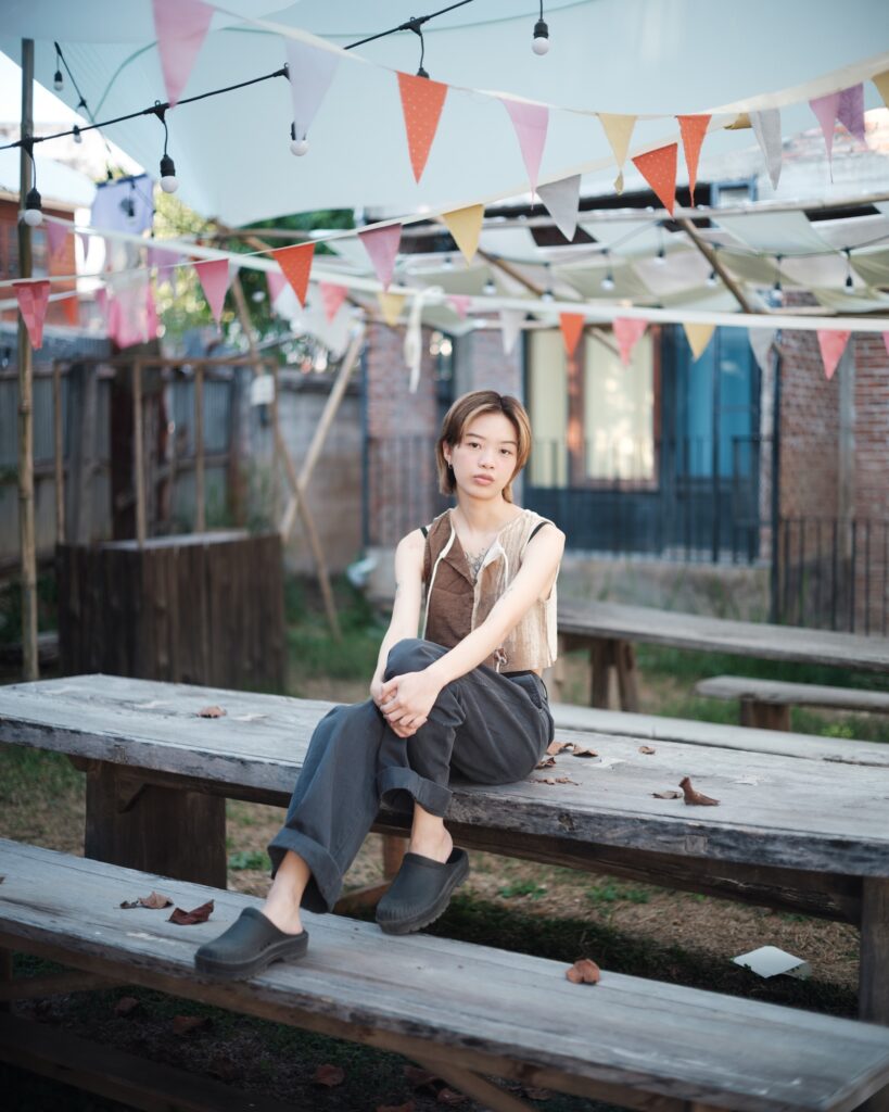 Kim seated on a wooden bench beneath colourful bunting