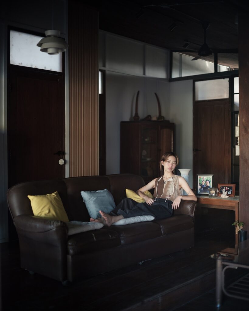 Kim reclining on a dark sofa in a wooden room