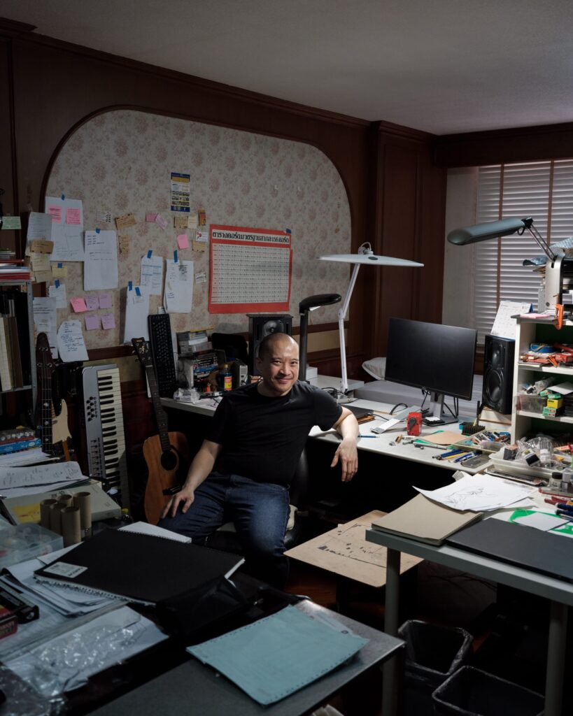 Parinot Kunakornwong seated at a desk surrounded by papers, equipment and a keyboard.