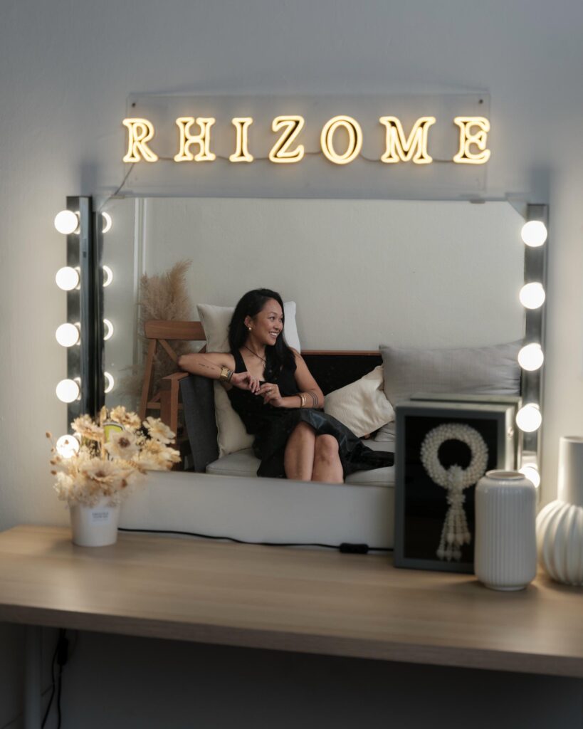 Ploy Phutpheng reflected in a dressing-table mirror beneath the Rhizome sign.