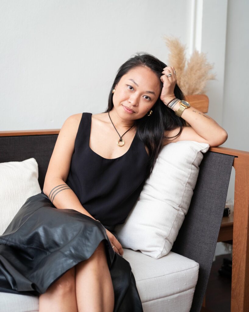 Ploy Phutpheng seated on a sofa with her head resting against one hand.
