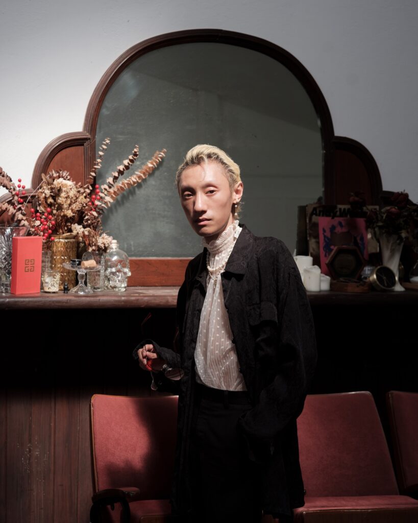Qooqoo standing beside an upright piano and a curved mirror