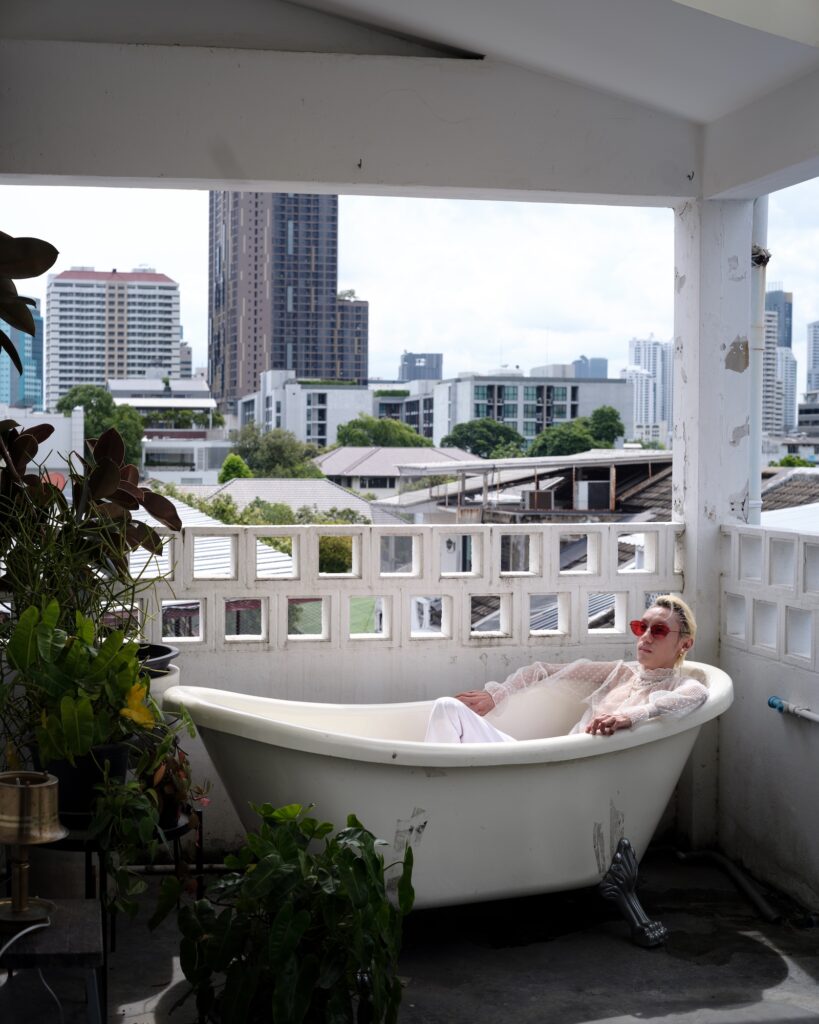 Qooqoo reclining in a freestanding bathtub on a balcony