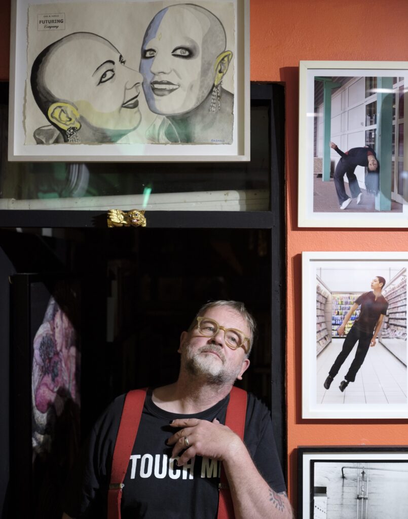 Reinhard wearing glasses and red braces, standing among framed artworks.