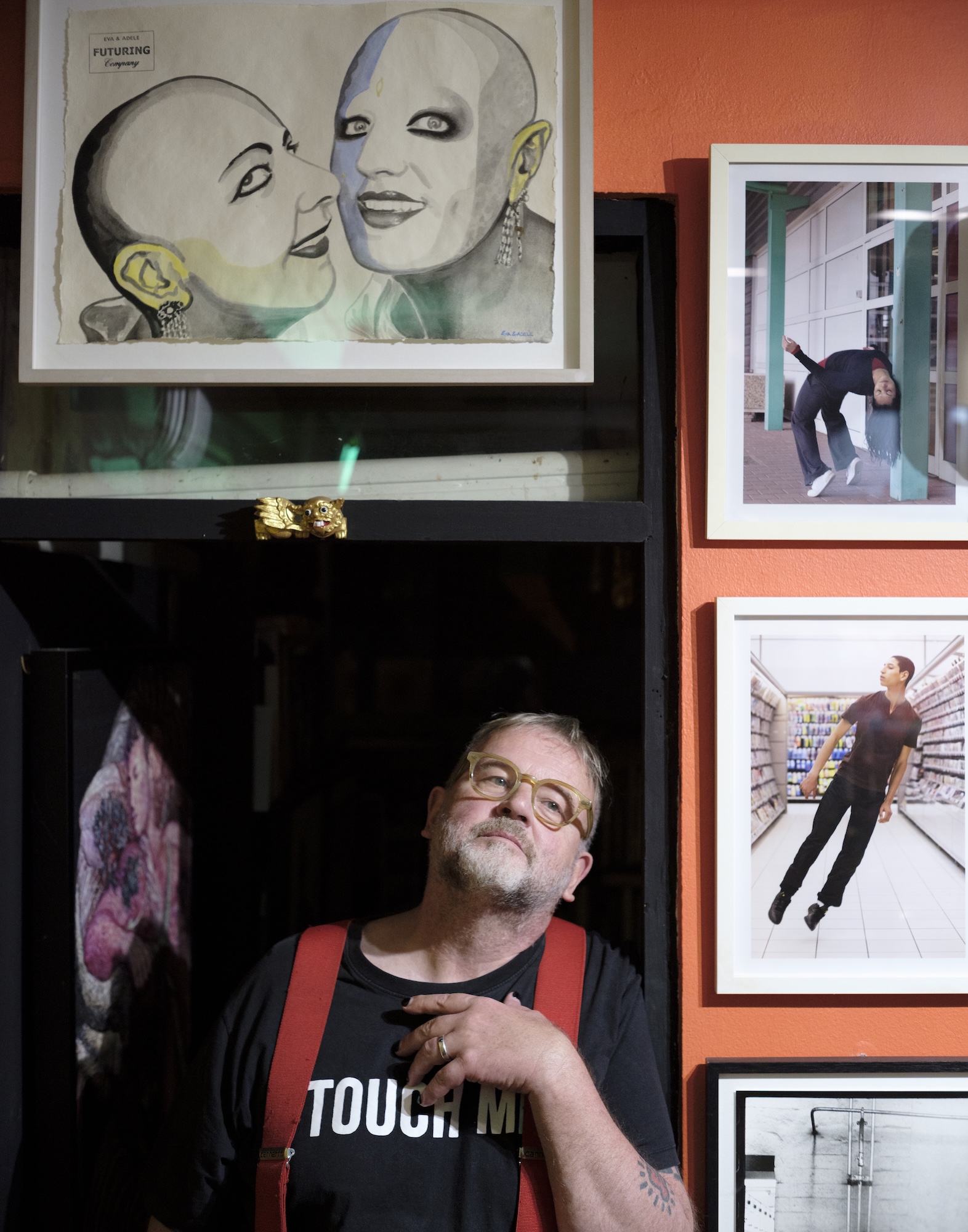 Reinhard wearing glasses and red braces, standing among framed artworks.