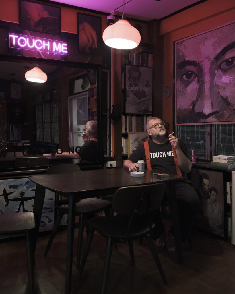 Reinhard seated at a table beneath a pink neon sign