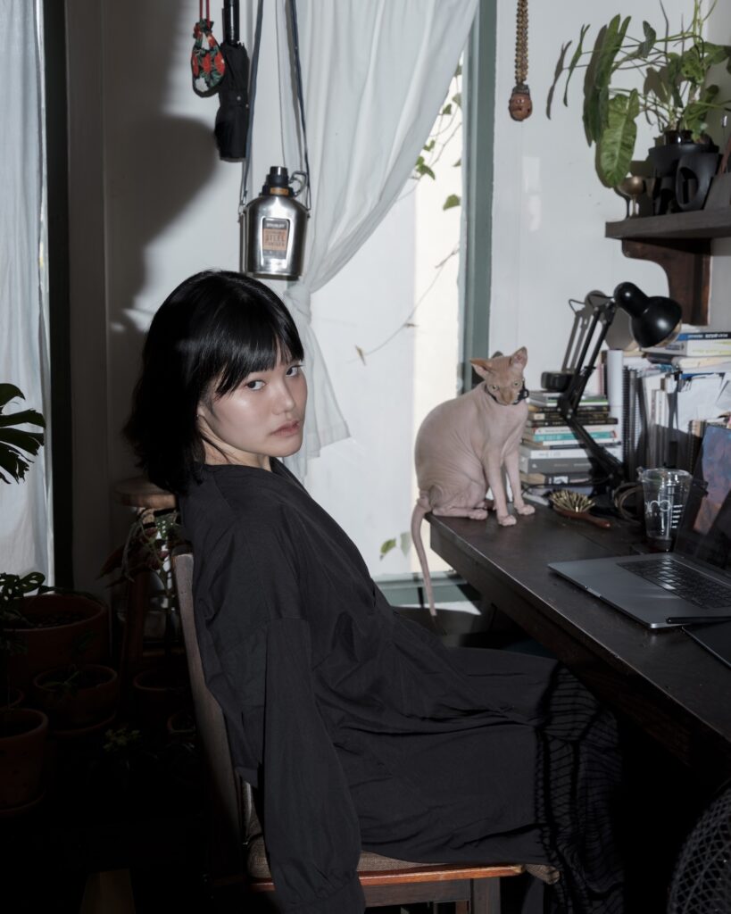 Rung seated beside a hairless cat at her apartment desk