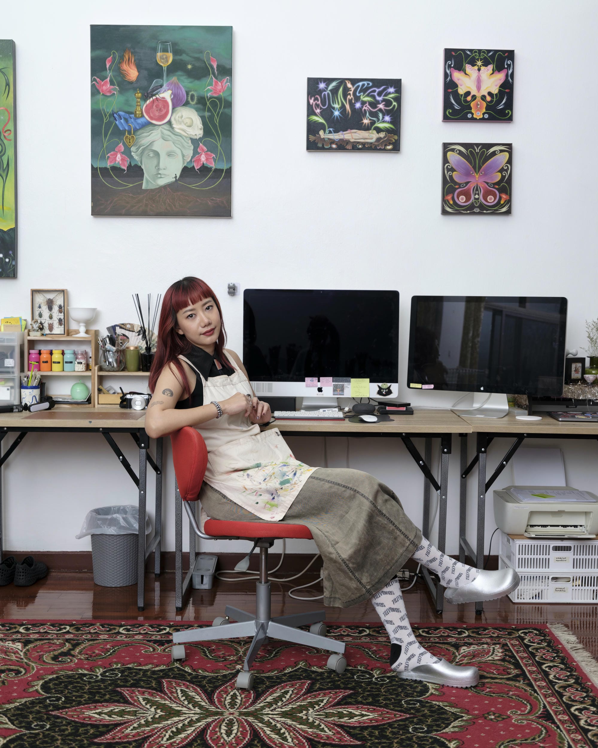 Sandy Chuchat seated at a computer desk beneath paintings in her Bangkok studio.