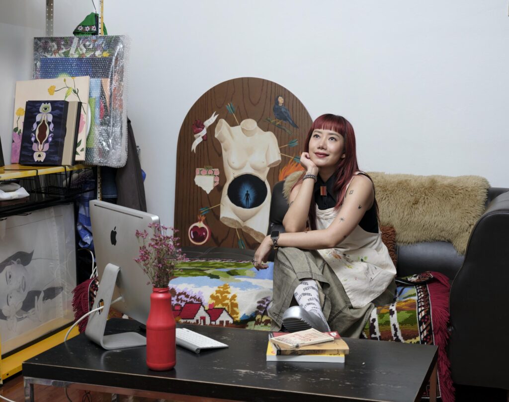 Sandy Chuchat seated on a sofa beside an oval painting and a computer.