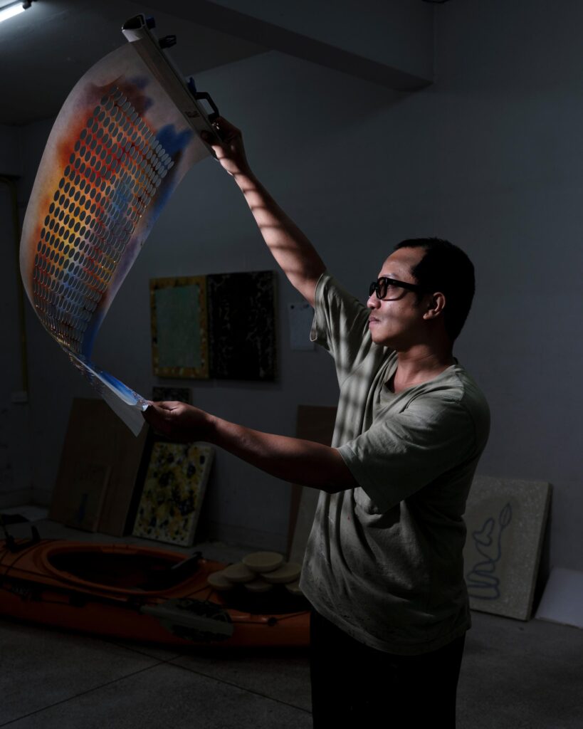 Tada Hengsapkul holding a large curved artwork above his head.