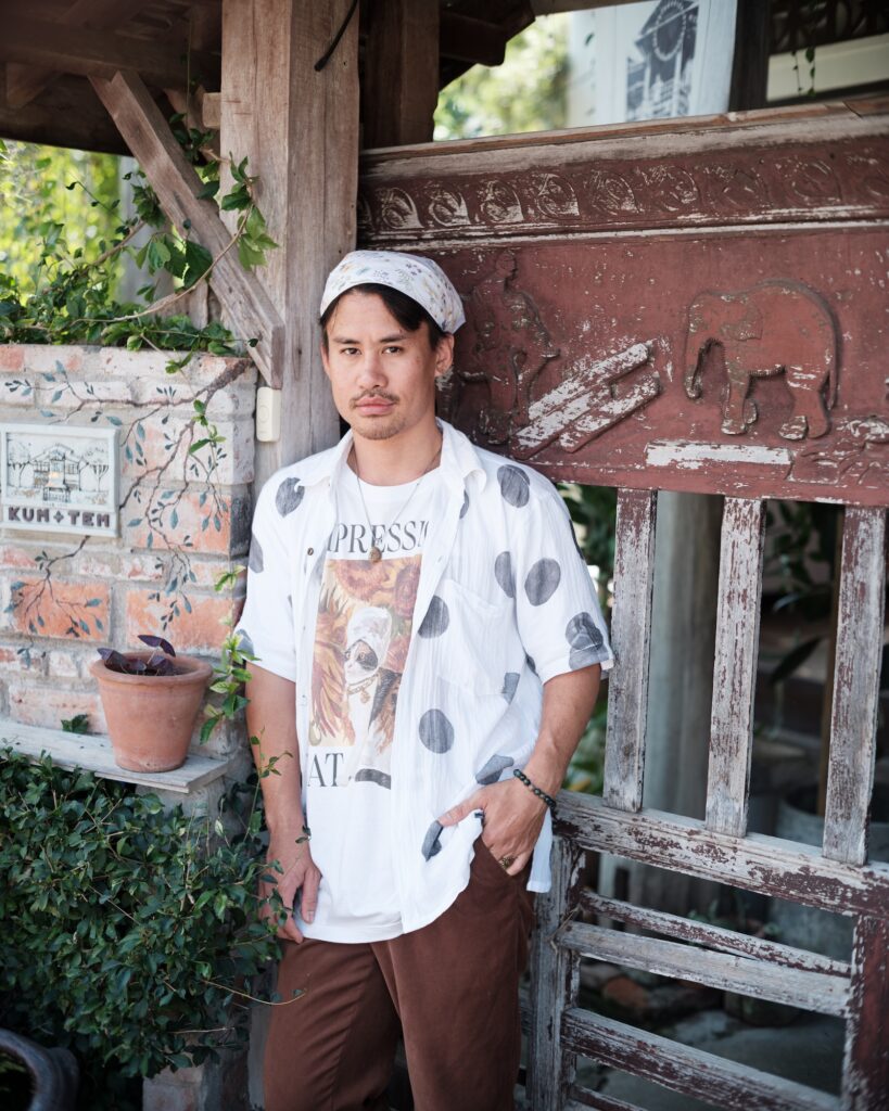 One of the Kum.tem House hosts standing beside an old wooden door