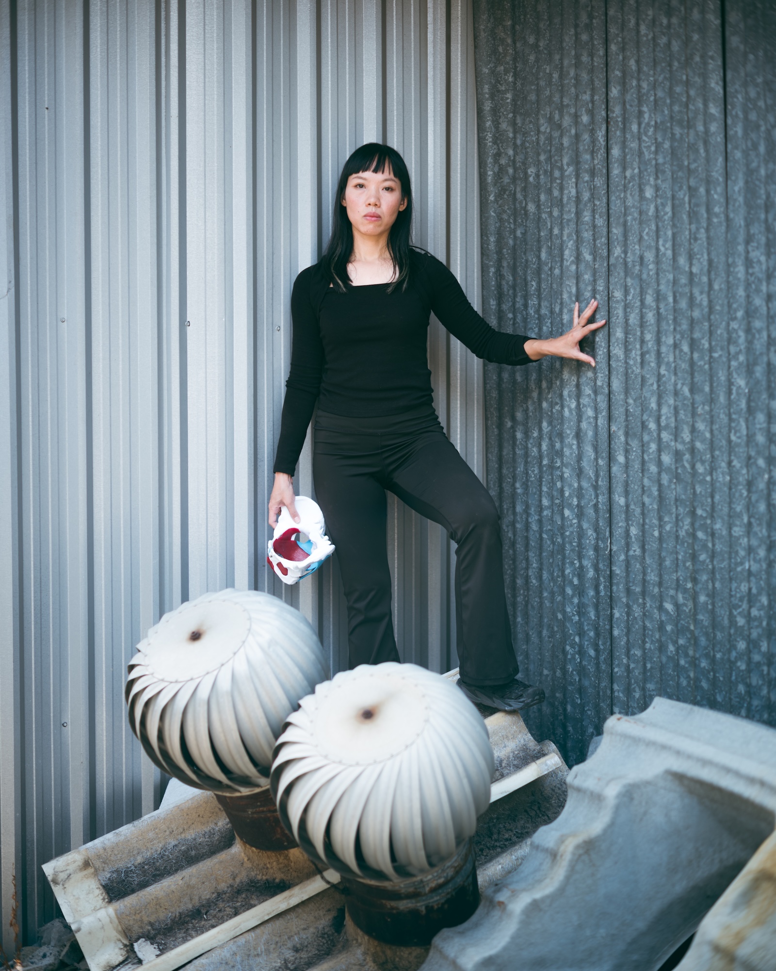 Wilawan in black clothes beside rooftop ventilators, holding an anatomical pelvis model.