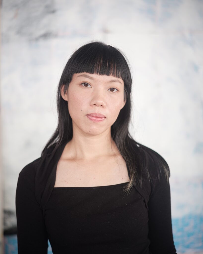 Close portrait of Wilawan wearing a black top against a pale wall.