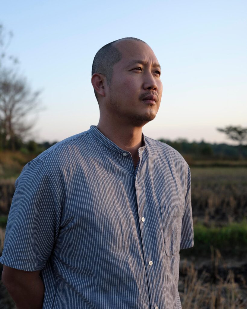 Alex Wang in a blue shirt beside a rice field near Phayao.