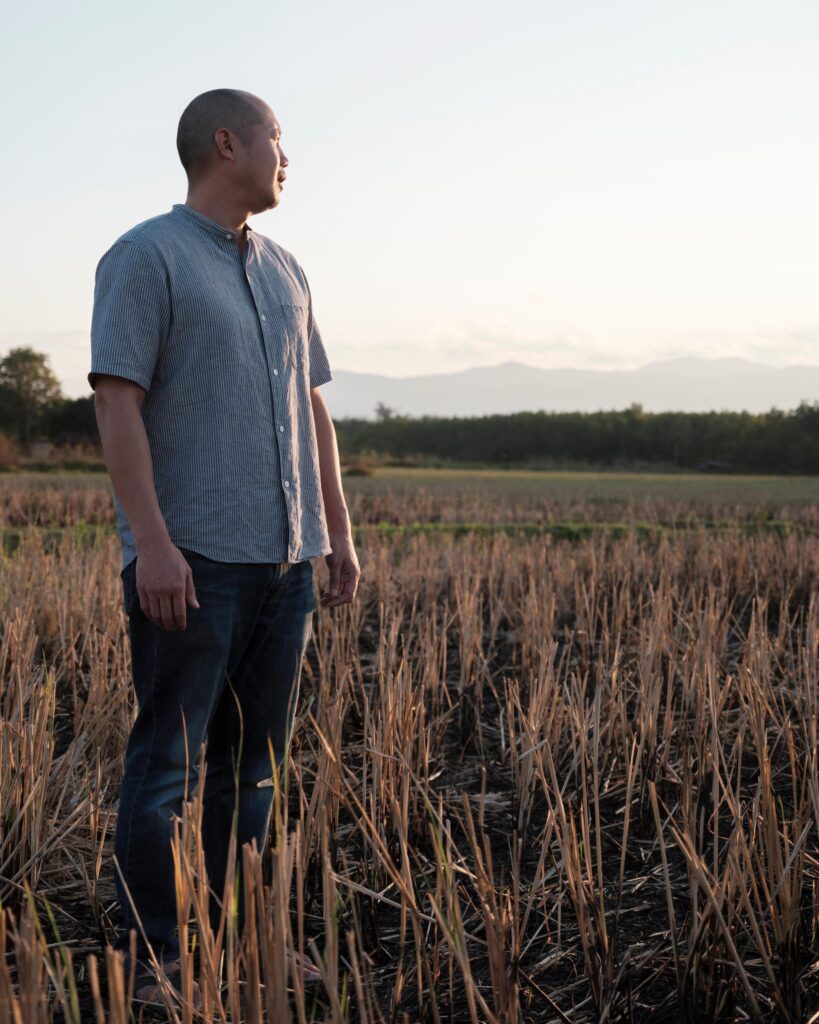 Alex Wang standing among cut rice stalks near Phayao at sunset.