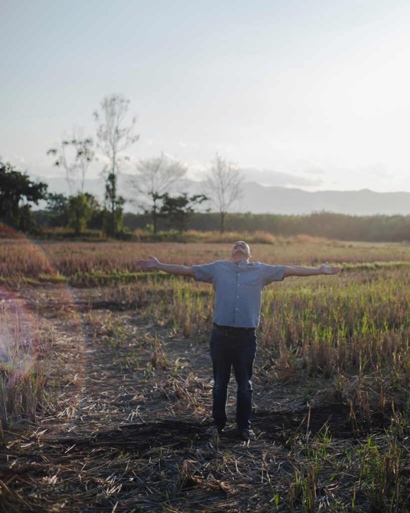 Alex Wang with arms outstretched in a rice field near Phayao.