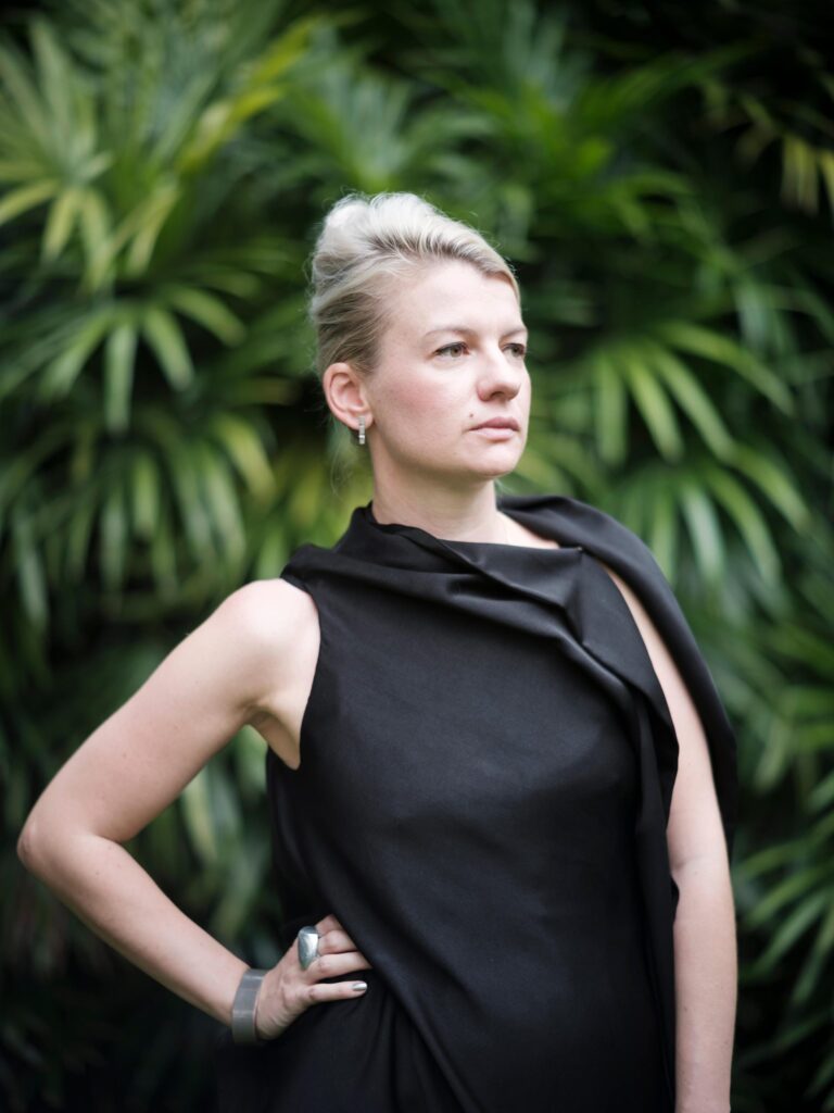 Alexandra Polyakova in a black dress against green foliage in Bangkok.