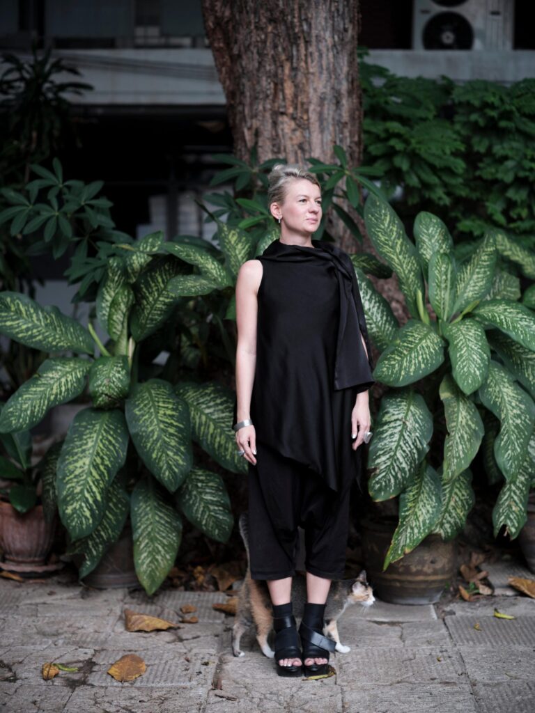 Alexandra Polyakova standing beside a tree and broad-leaved plants in Bangkok.