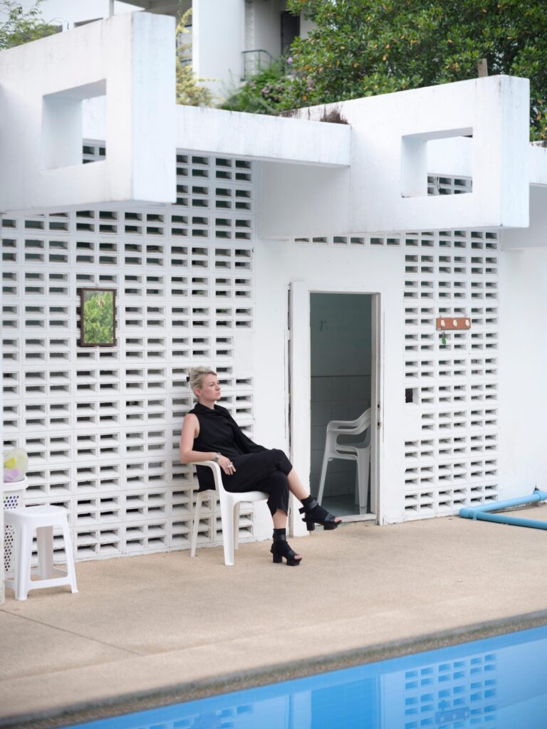 Alexandra Polyakova seated beside a swimming pool and white breeze-block wall in Bangkok.