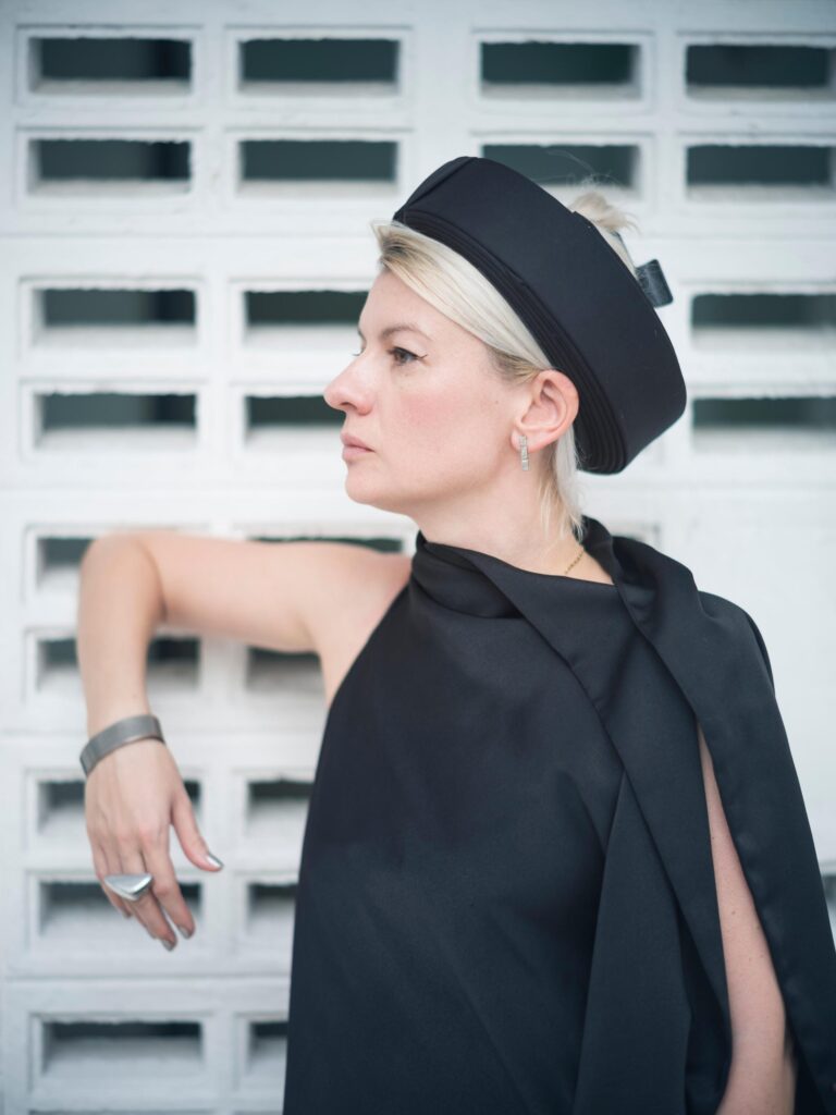 Alexandra Polyakova wearing a black hat beside a white breeze-block wall in Bangkok.