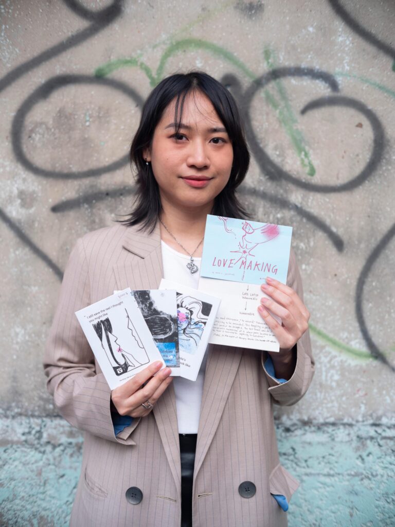 Member of Zua, Cinema and Chalan holding several publications beside a graffiti-covered wall in Bangkok.