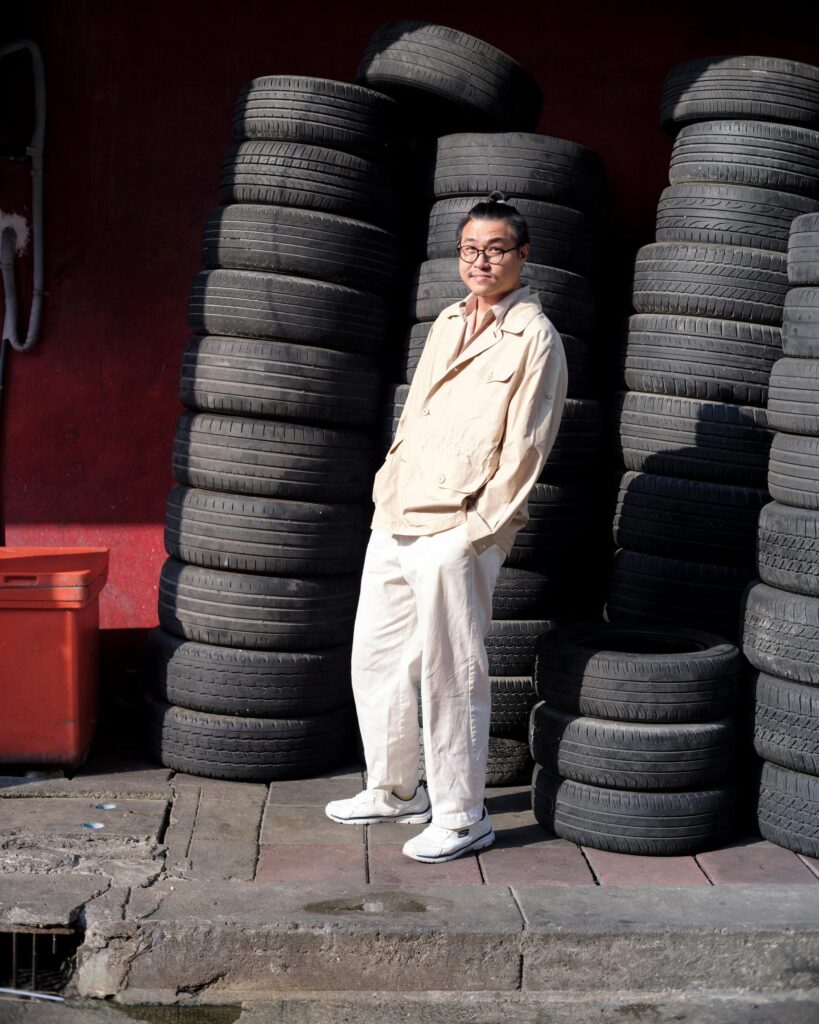 Member of Zua, Cinema and Chalan standing in front of stacked tyres in Bangkok.