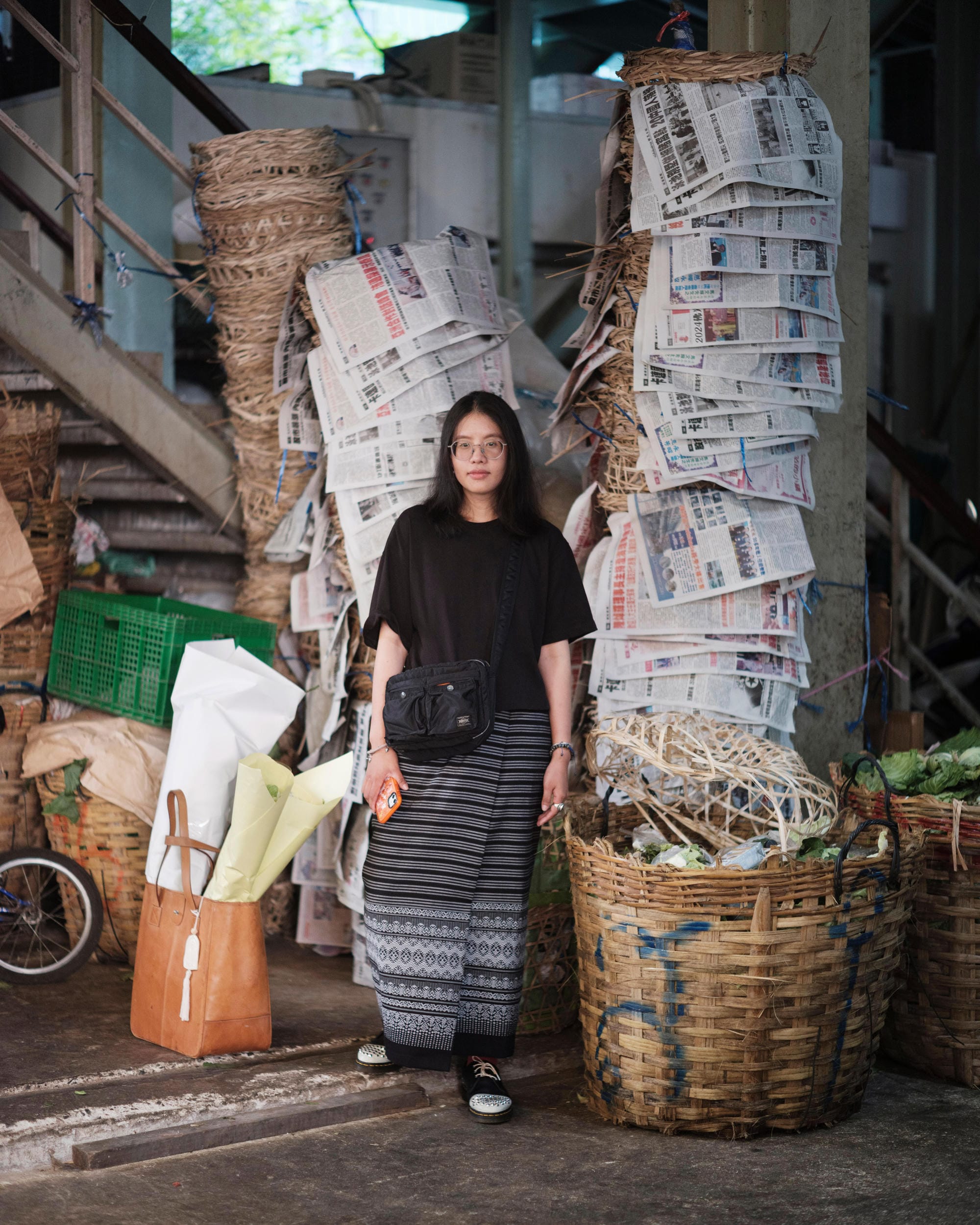 Ayre Wongchaksu standing beside baskets and stacked newspapers at a Bangkok flower market.
