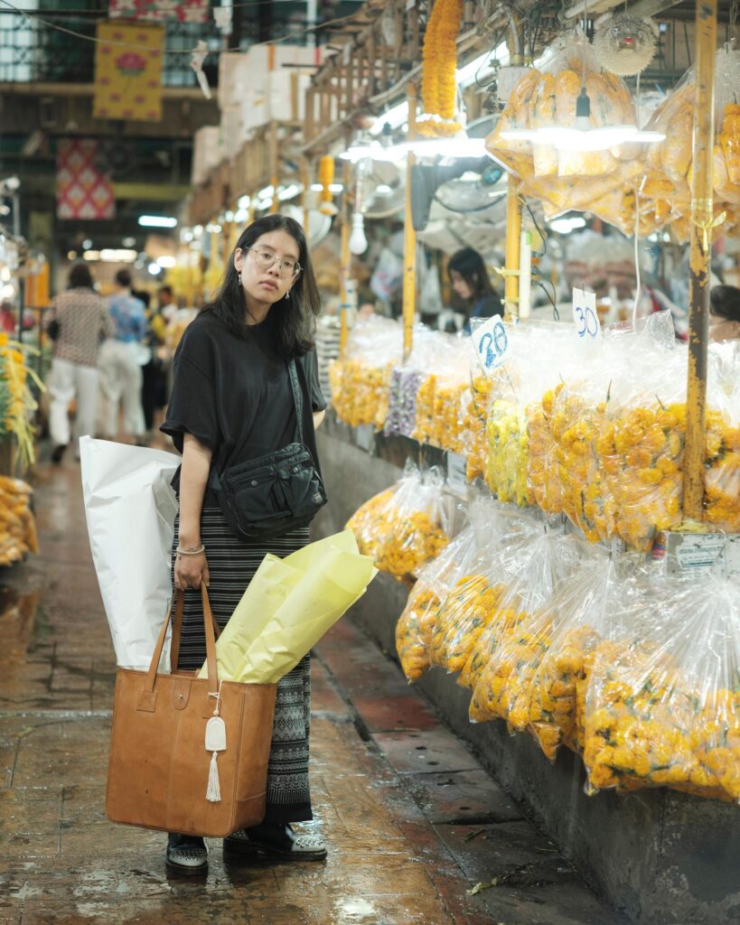 Ayre Wongchaksu carrying flowers beside garland stalls at Pak Klong Talat, Bangkok.