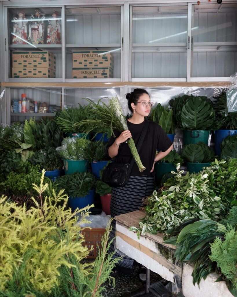 Ayre Wongchaksu holding green stems beside plant stalls in Bangkok.
